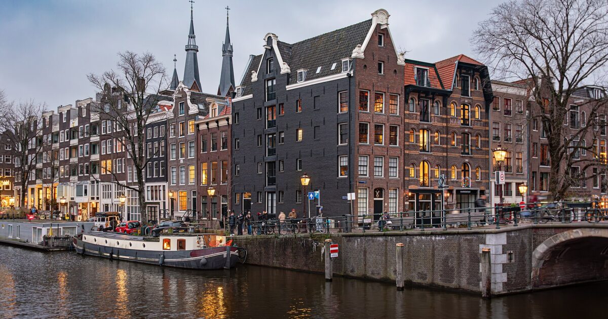 An Amsterdam canal at dusk with a moored boat, gabled houses and a bridge