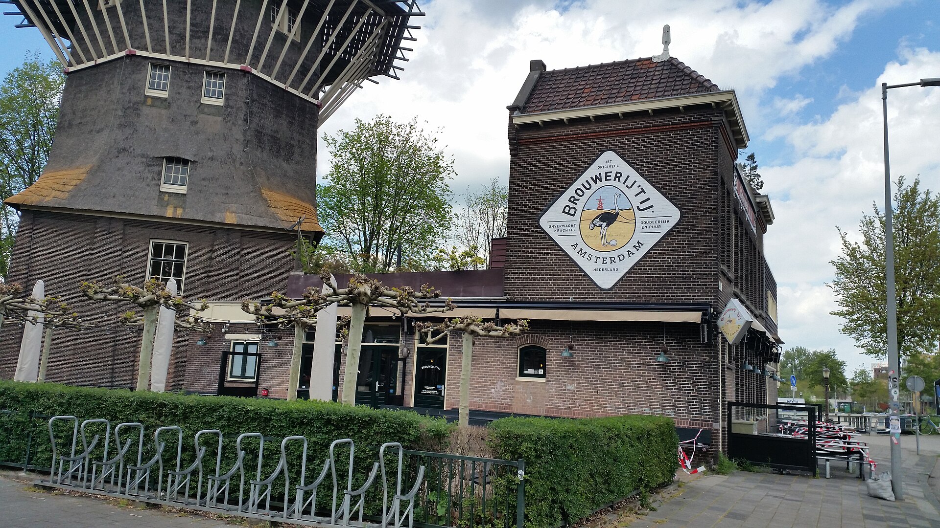 Brouwerij t IJ beside the base of De Gooyer windmill in Amsterdam, with a brewery sign and empty bicycle racks.