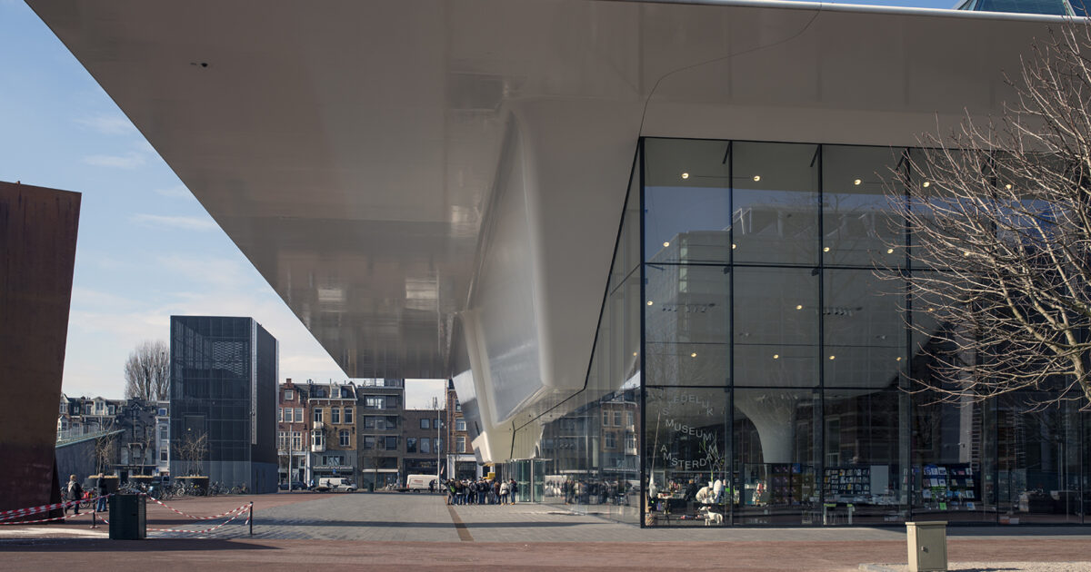 The Stedelijk Museum's white Bathtub extension projects over its glass ground floor beside the paved Museumplein in Amsterdam.