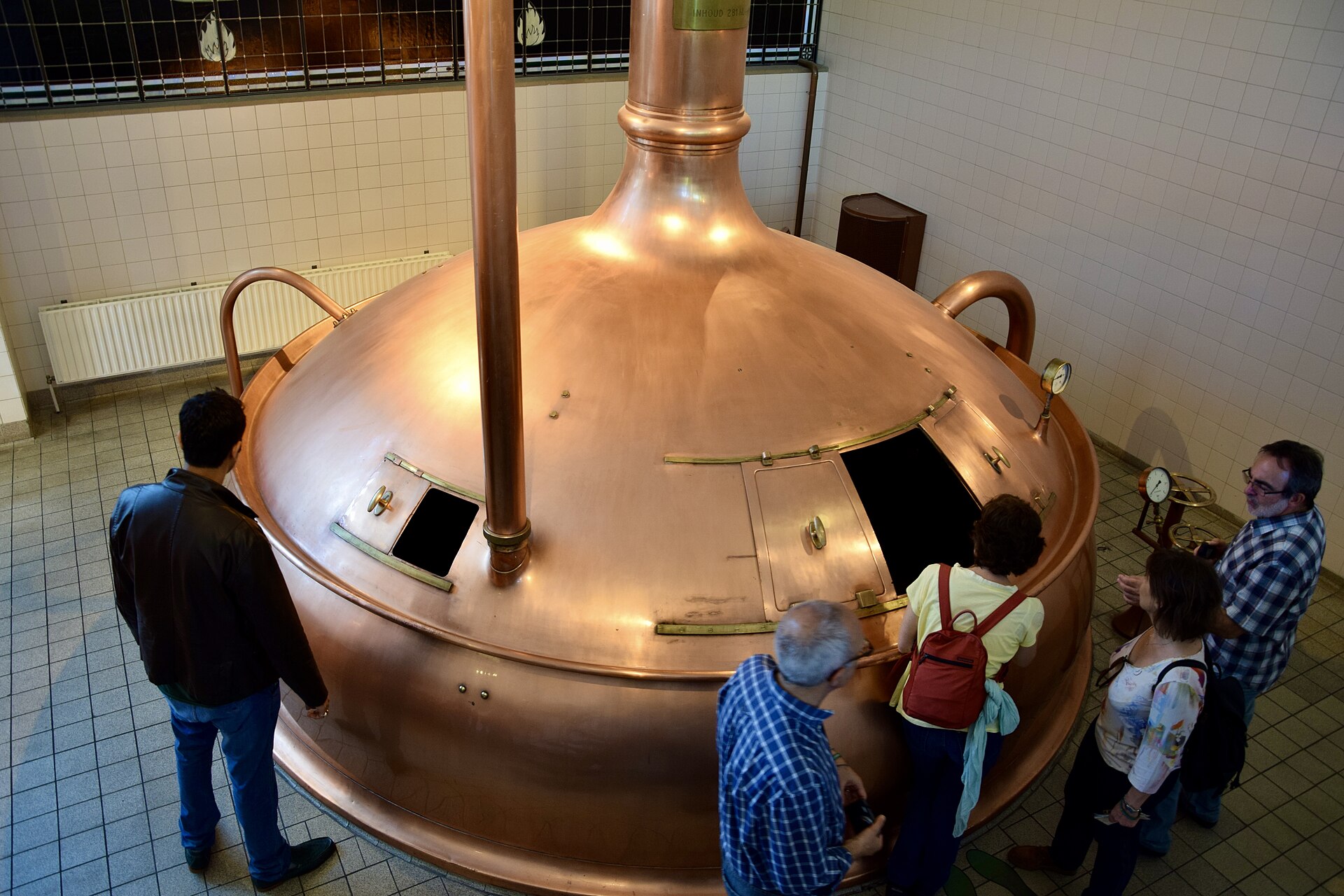 Visitors examine a large copper brewing kettle with an open hatch inside the tiled Heineken Experience in Amsterdam.